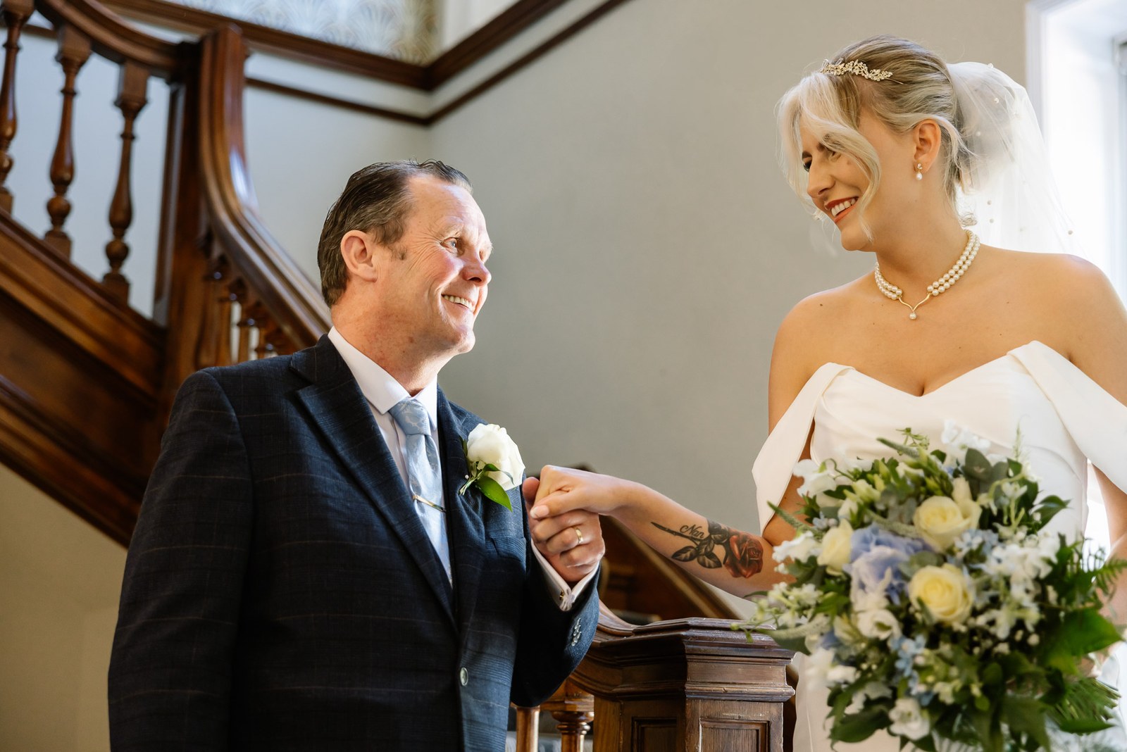 The father of the bride holding her hand on the timber staircase