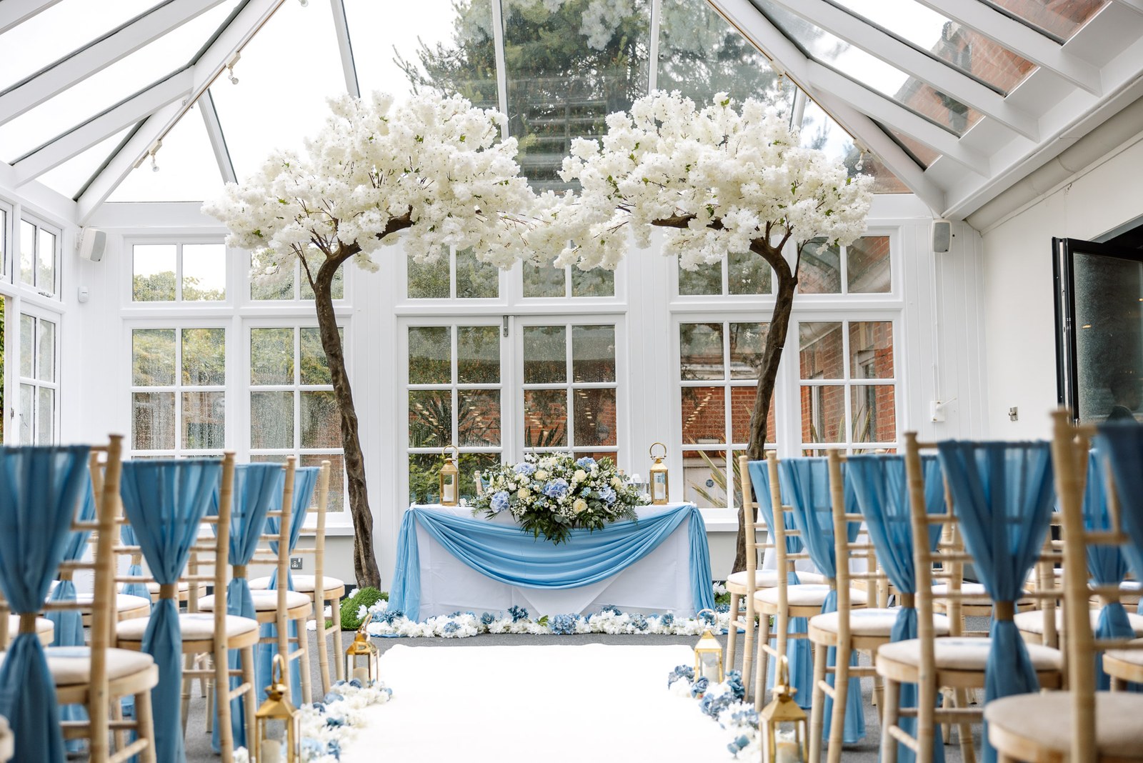 The orangery ceremony room set with blossom trees and blue-sashed chairs at Hunton Park Hotel