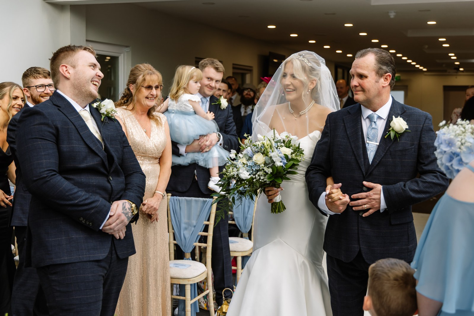 The bride arriving on her father's arm as guests turn to watch