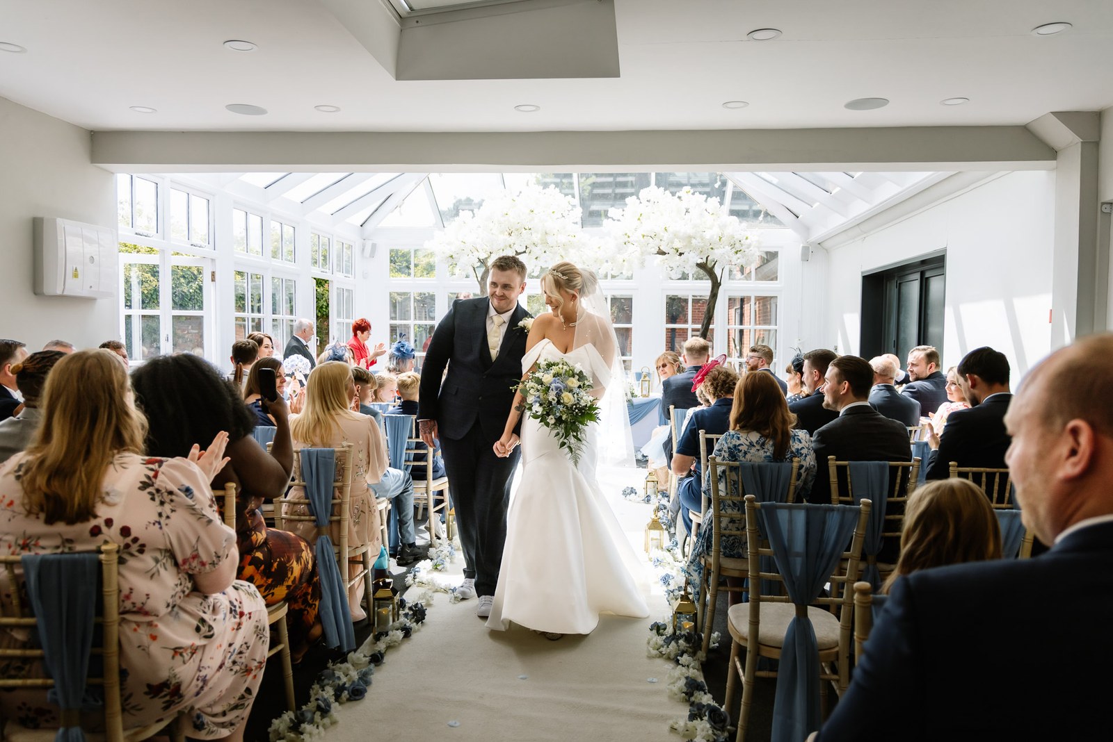 The newlyweds walking back down the aisle through the blossom-lined orangery