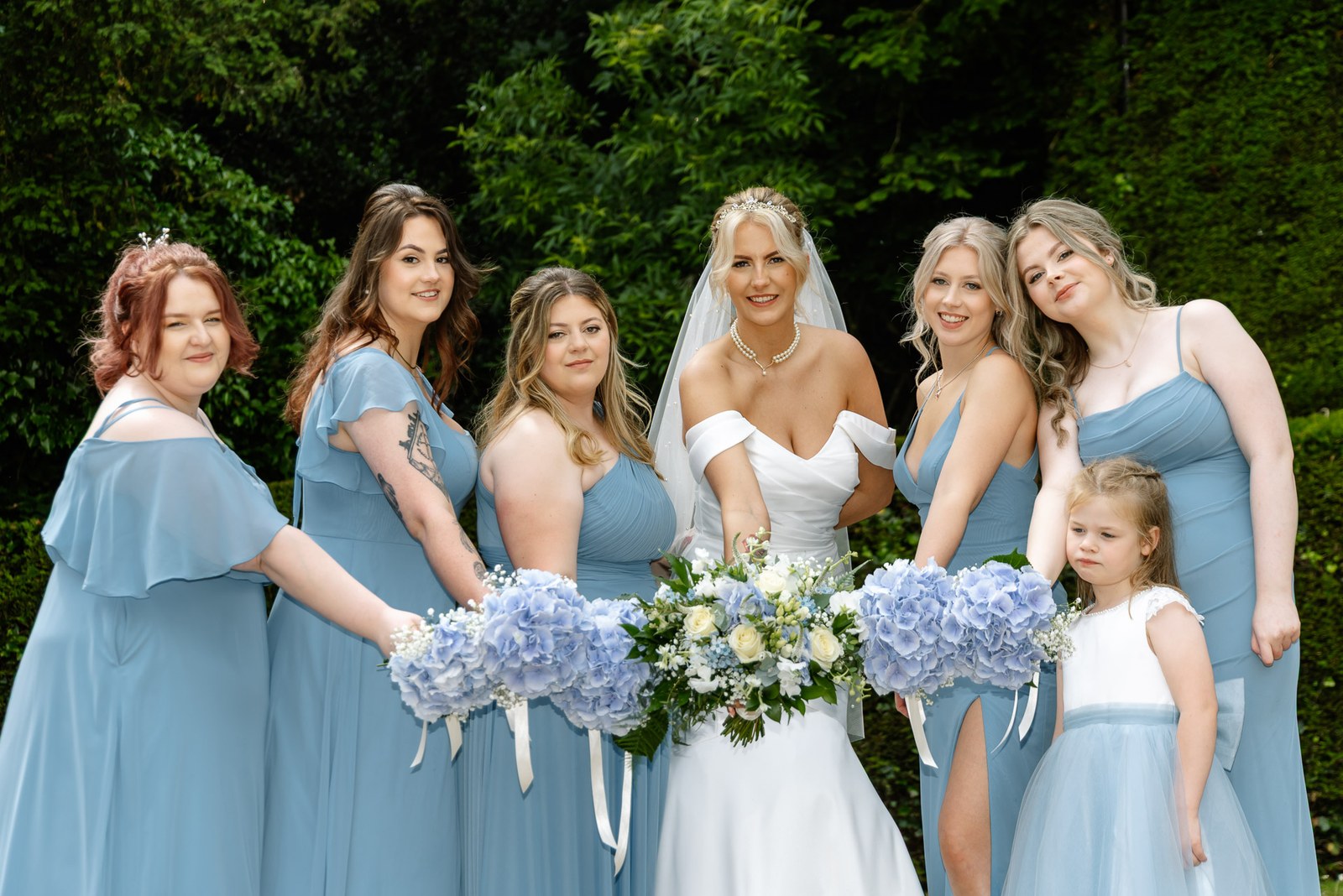 The bride with her bridesmaids and flower girl holding blue hydrangea bouquets