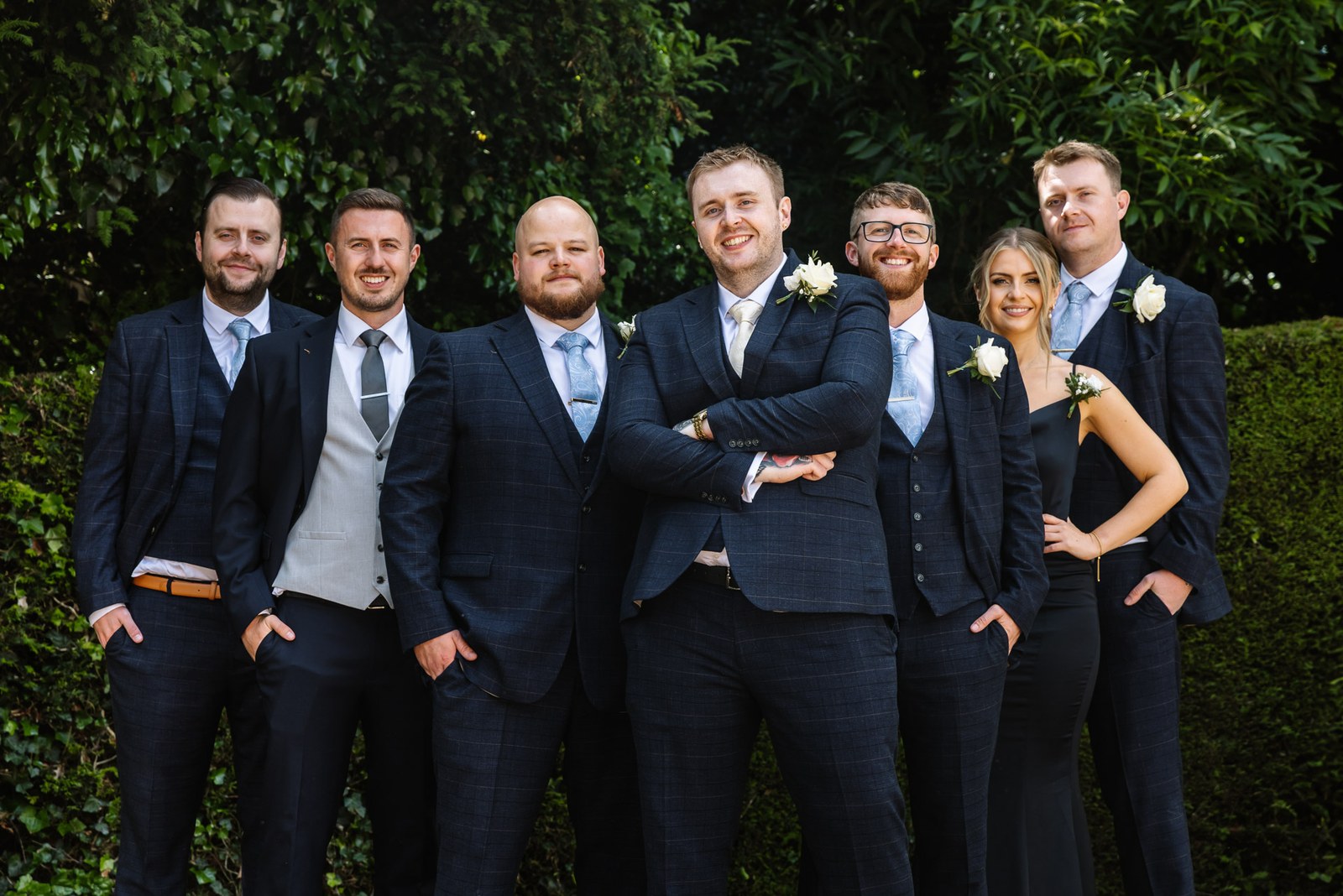 The groom with his groomsmen gathered by the garden hedge