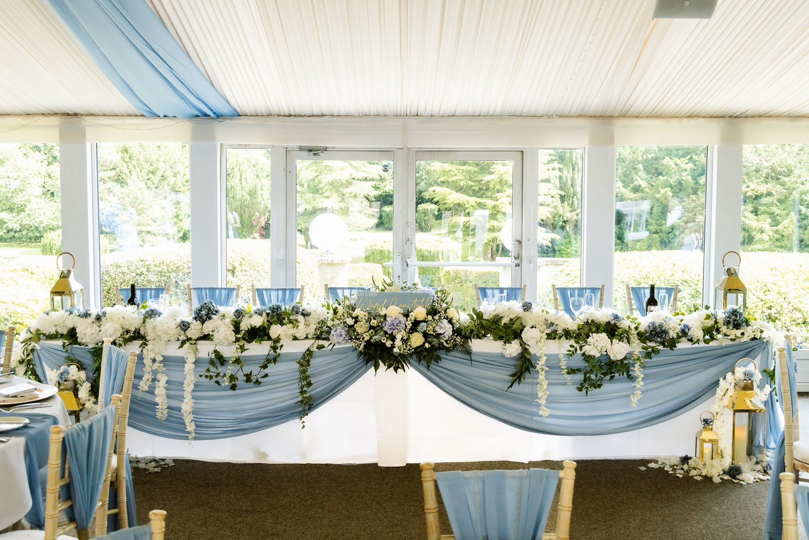 The top table dressed with blue drapes and a floral garland beneath the marquee ceiling