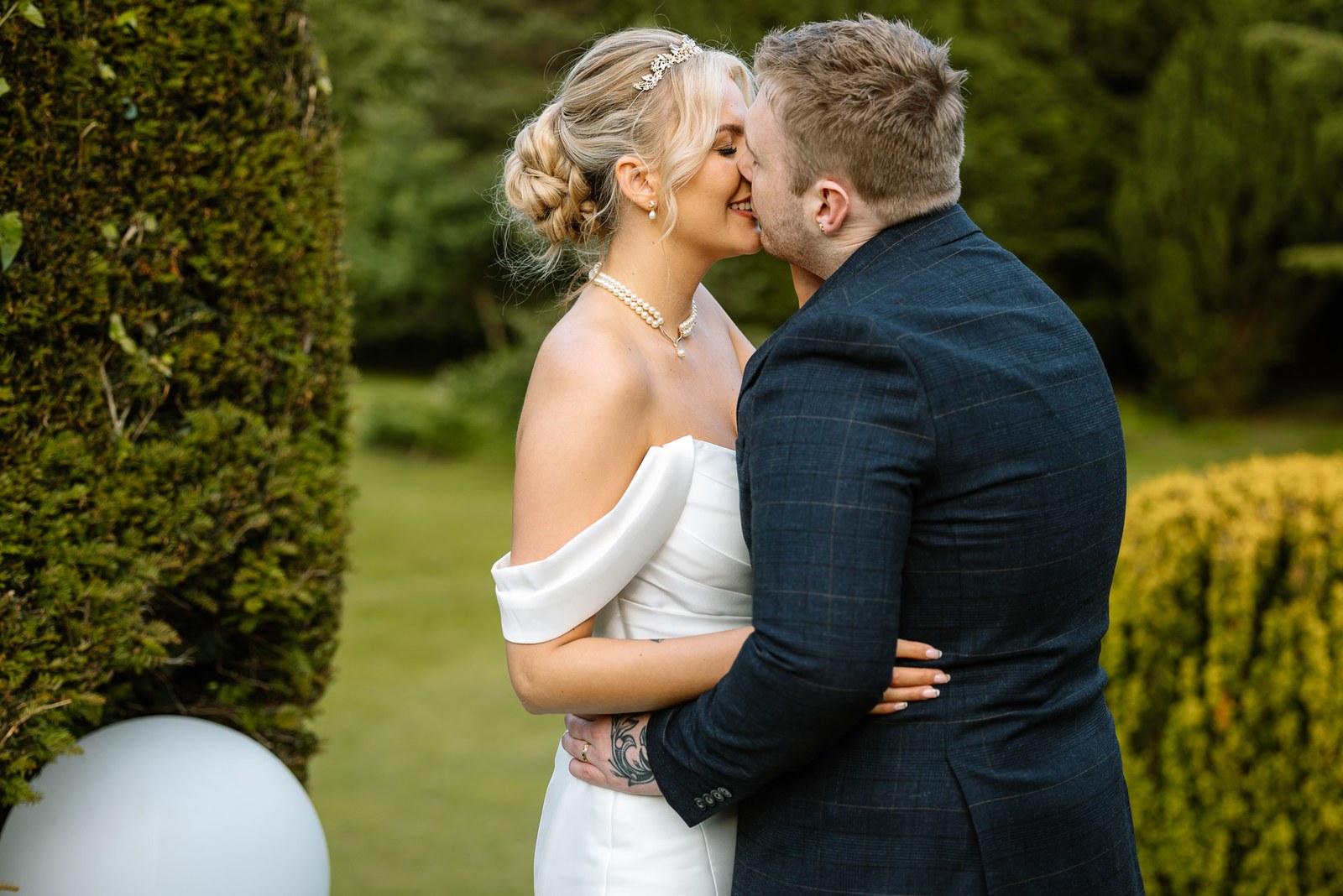 Bride and groom kissing among the clipped topiary in the gardens