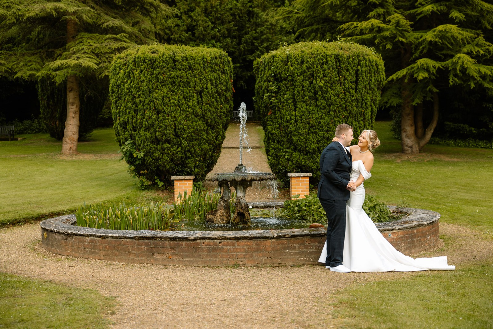 Bride and groom beside a fountain in the topiary garden at Hunton Park Hotel