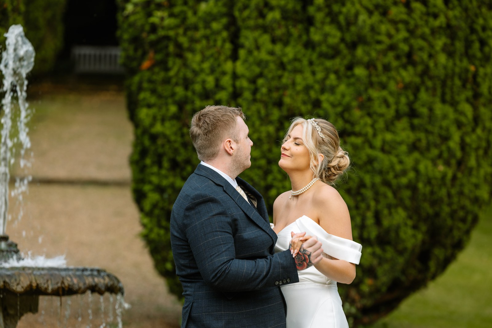 The couple by the garden fountain framed by tall yew hedges
