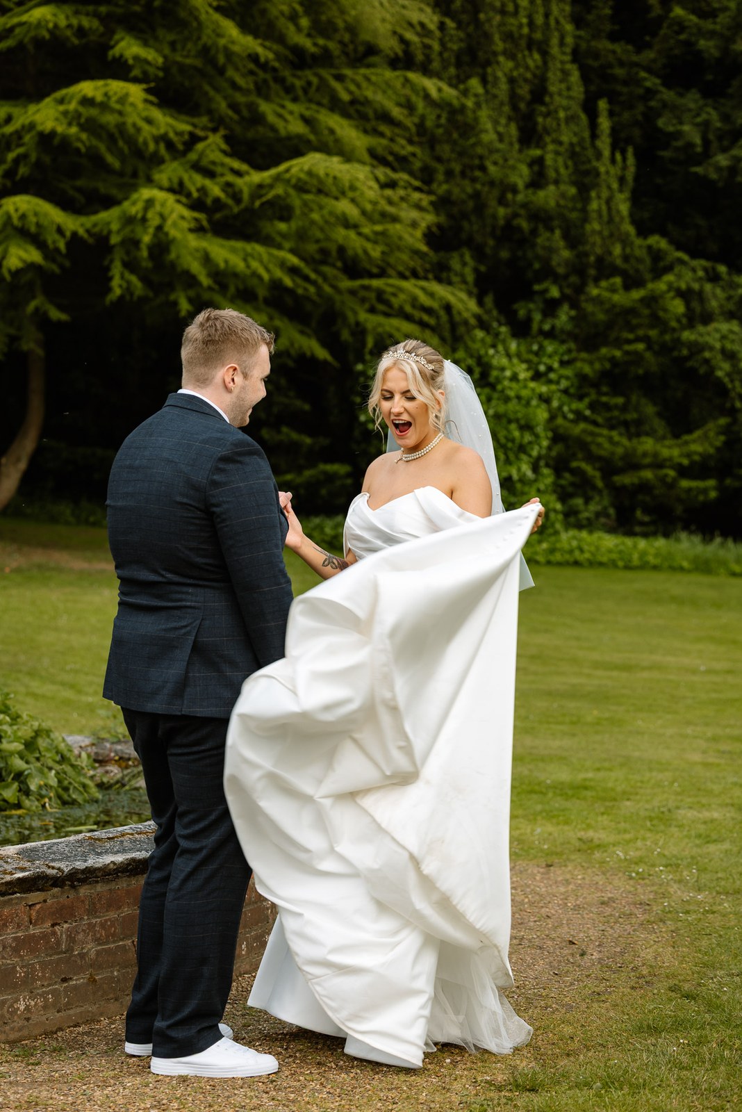 The bride swishing her gown as the couple pose on the lawn