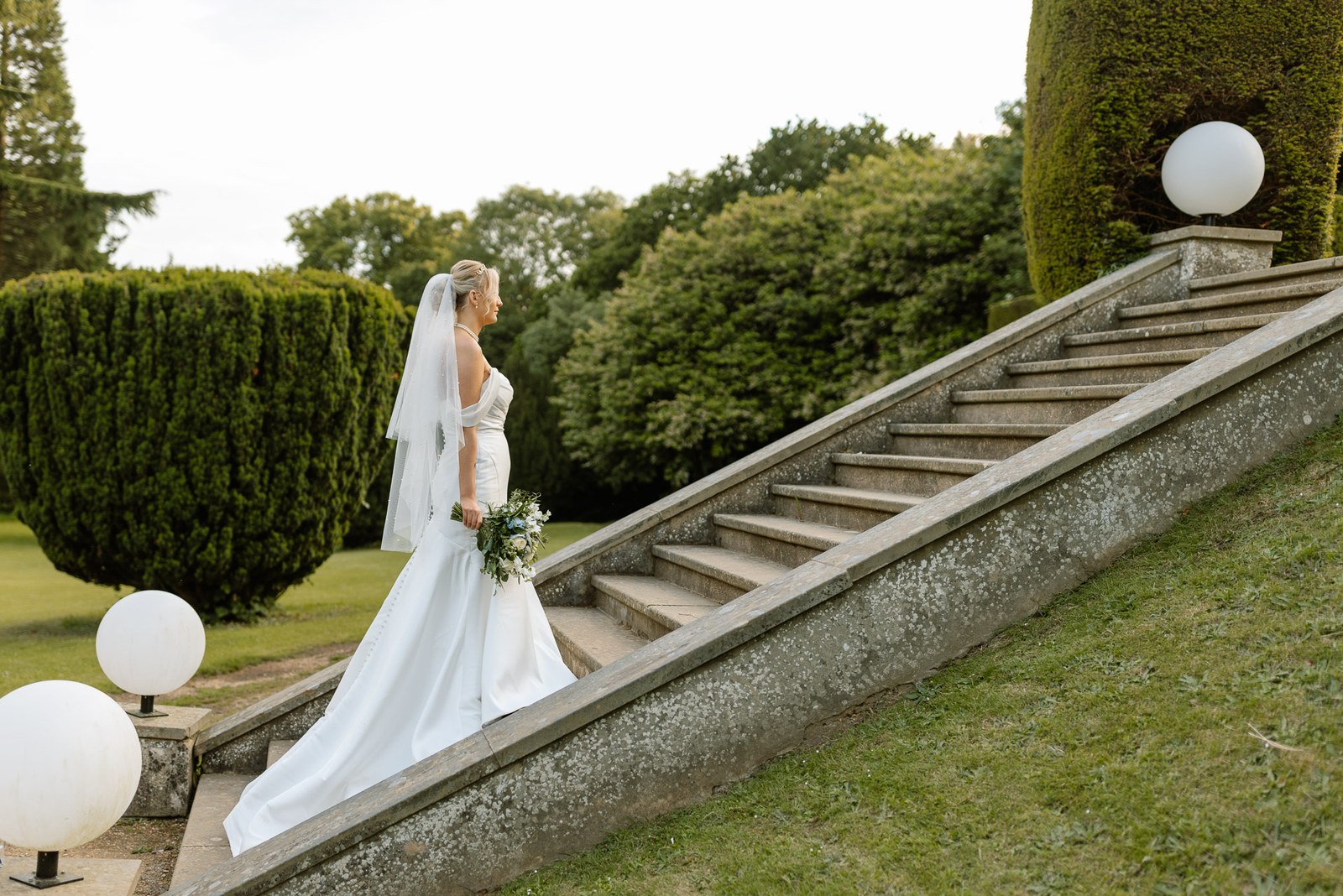 The bride ascending the grand stone garden steps flanked by globe lamps at Hunton Park Hotel