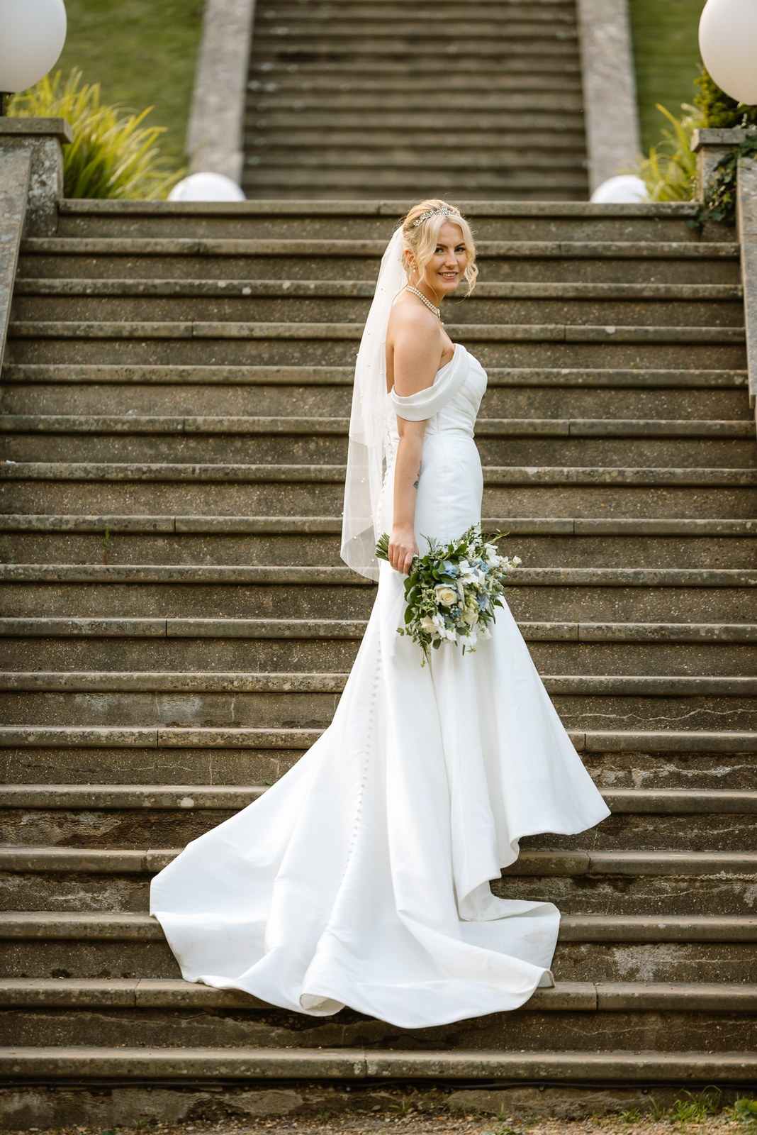 Full-length portrait of the bride posed on the sweeping stone garden staircase