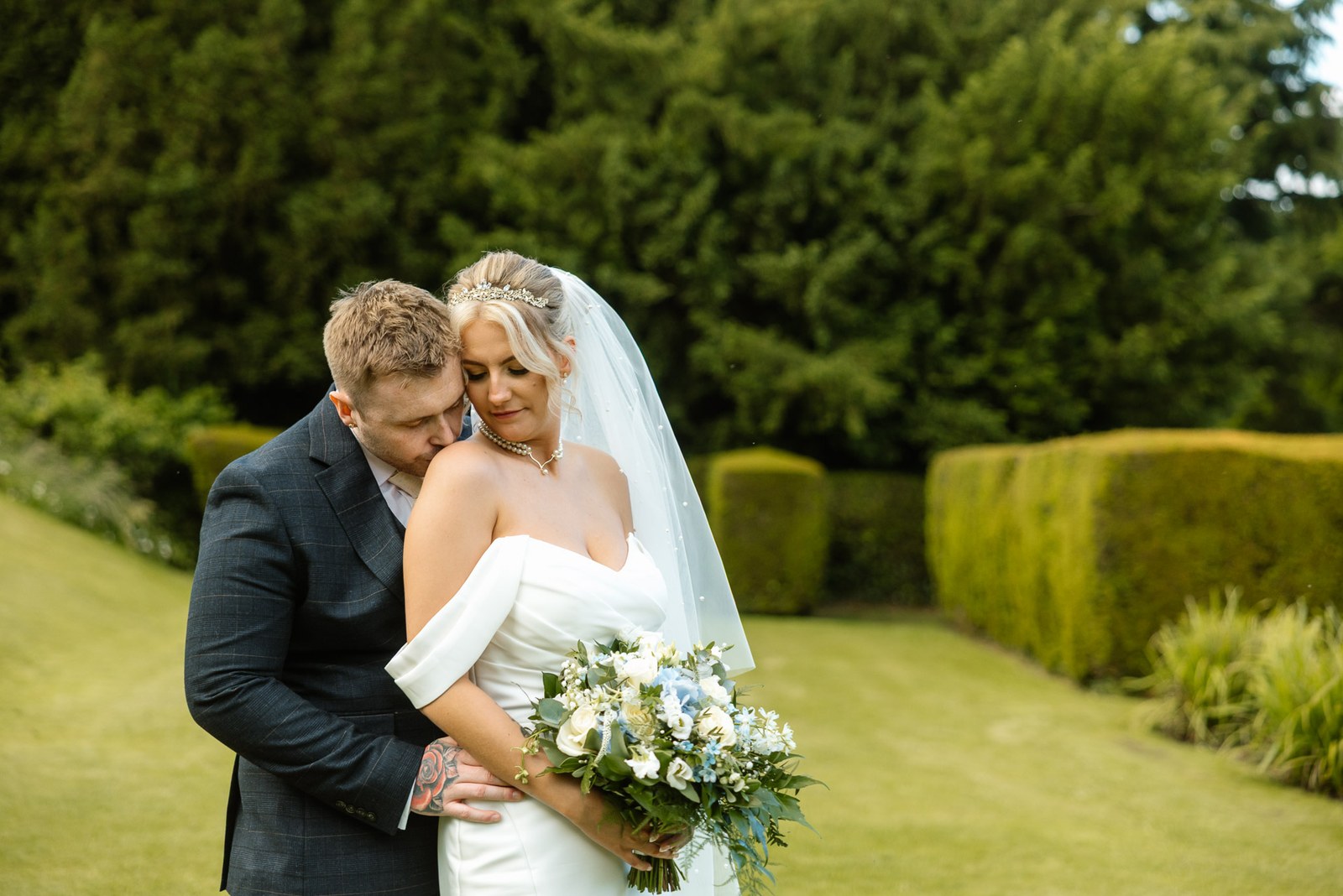 The groom kissing the bride's shoulder in a garden embrace