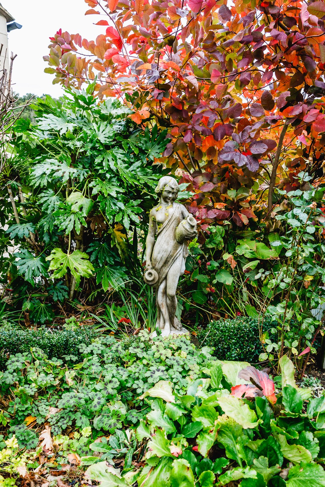 A weathered garden statue tucked among autumn foliage in the grounds