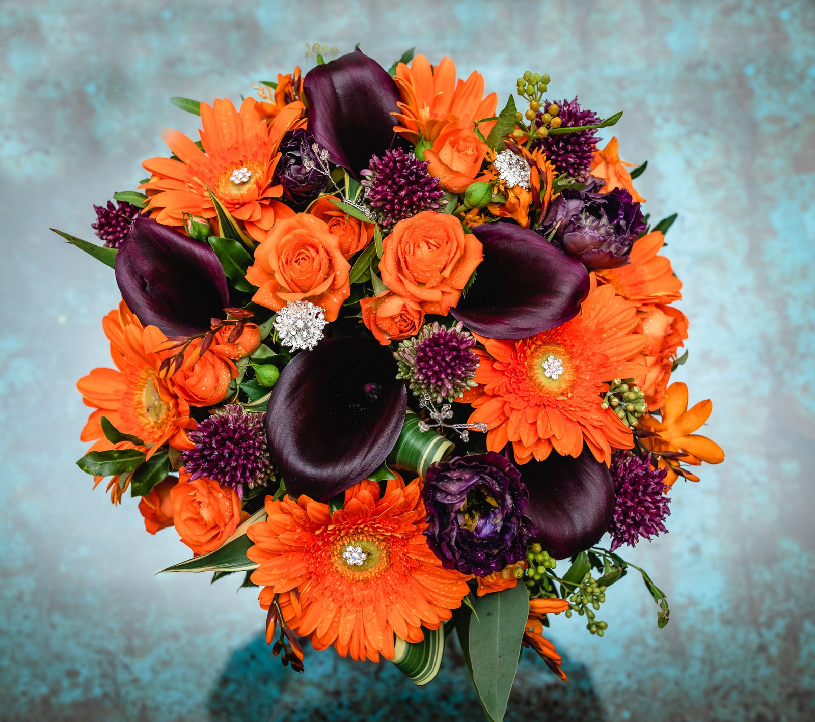 A vibrant bouquet of orange gerberas, roses and deep aubergine calla lilies