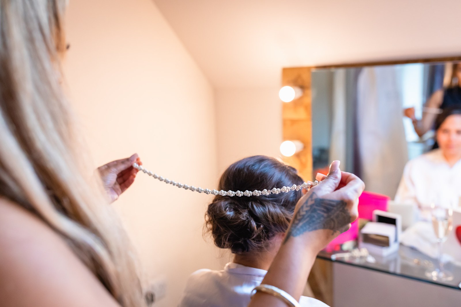A jewelled hair vine being set in the bride's hair, caught in the mirror