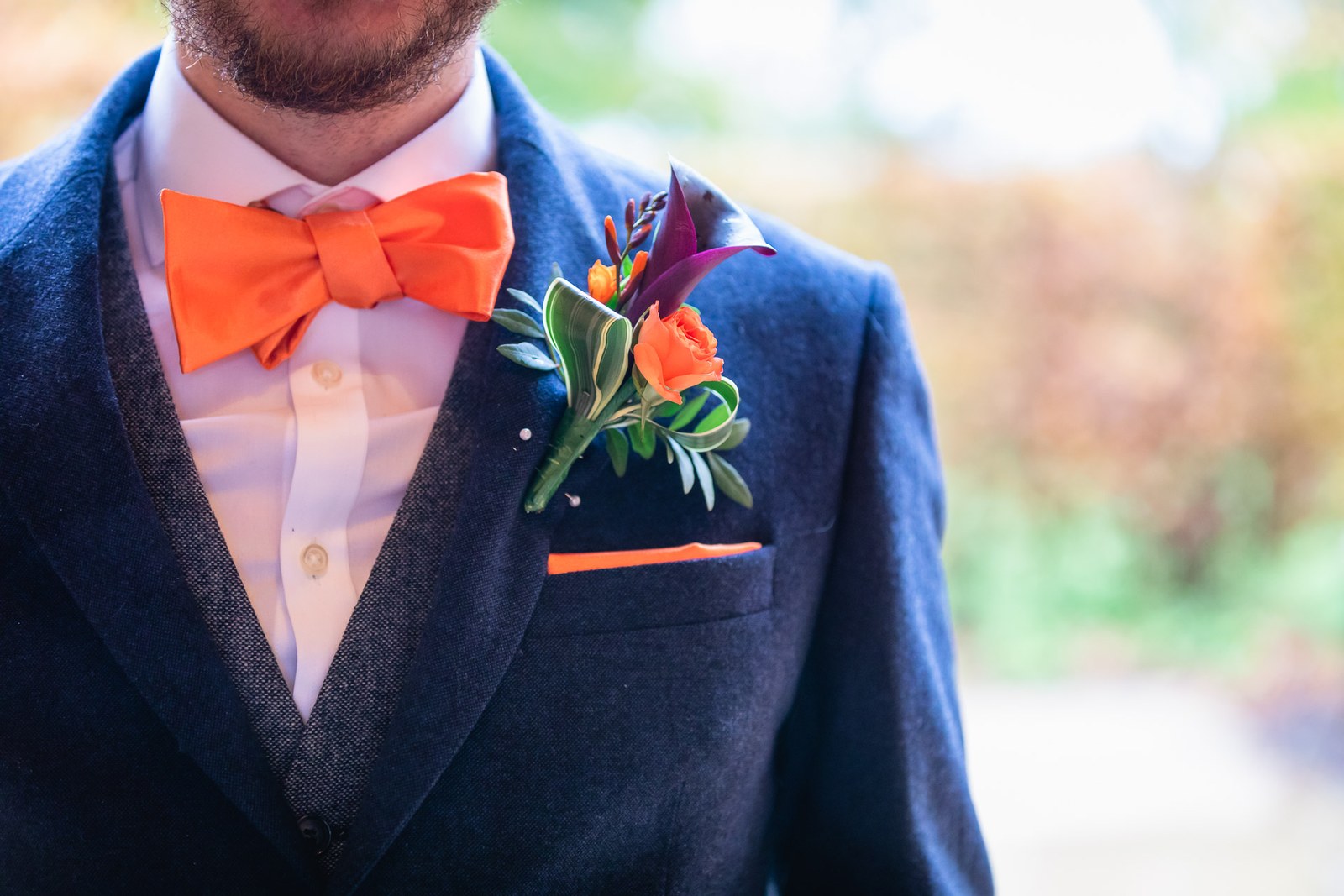 Close-up of the groom's navy tweed lapel with an orange bow tie and bright buttonhole