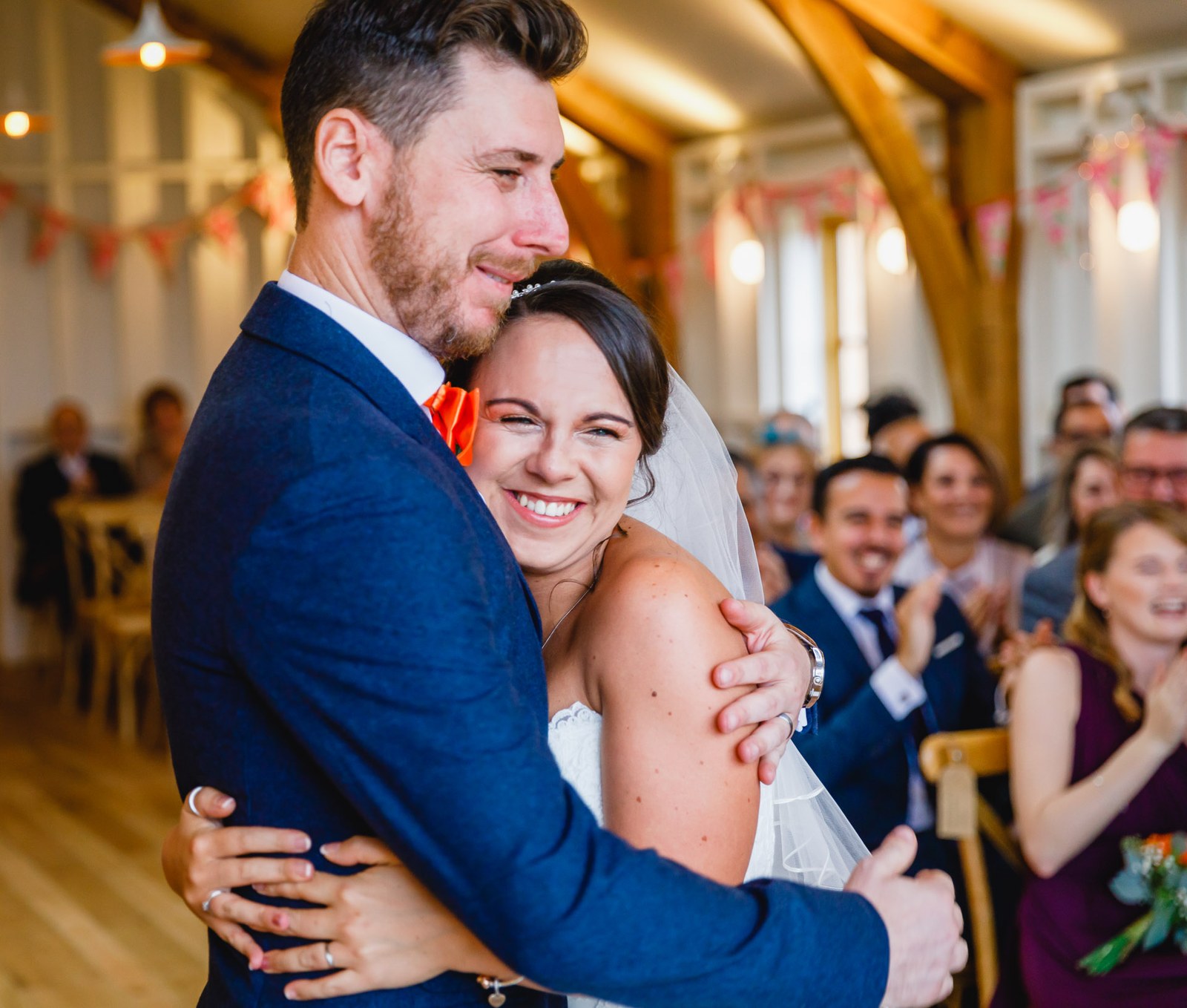 Bride and groom in a happy embrace with guests seated behind