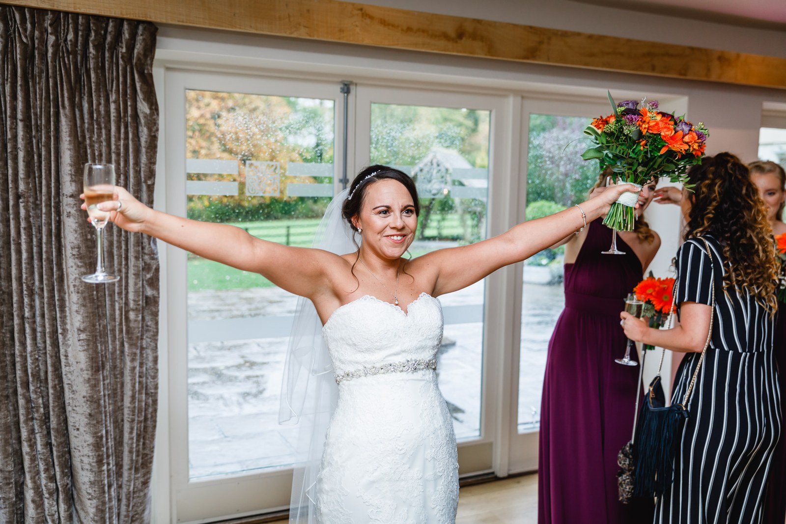 The bride raising her bouquet and a glass by the window