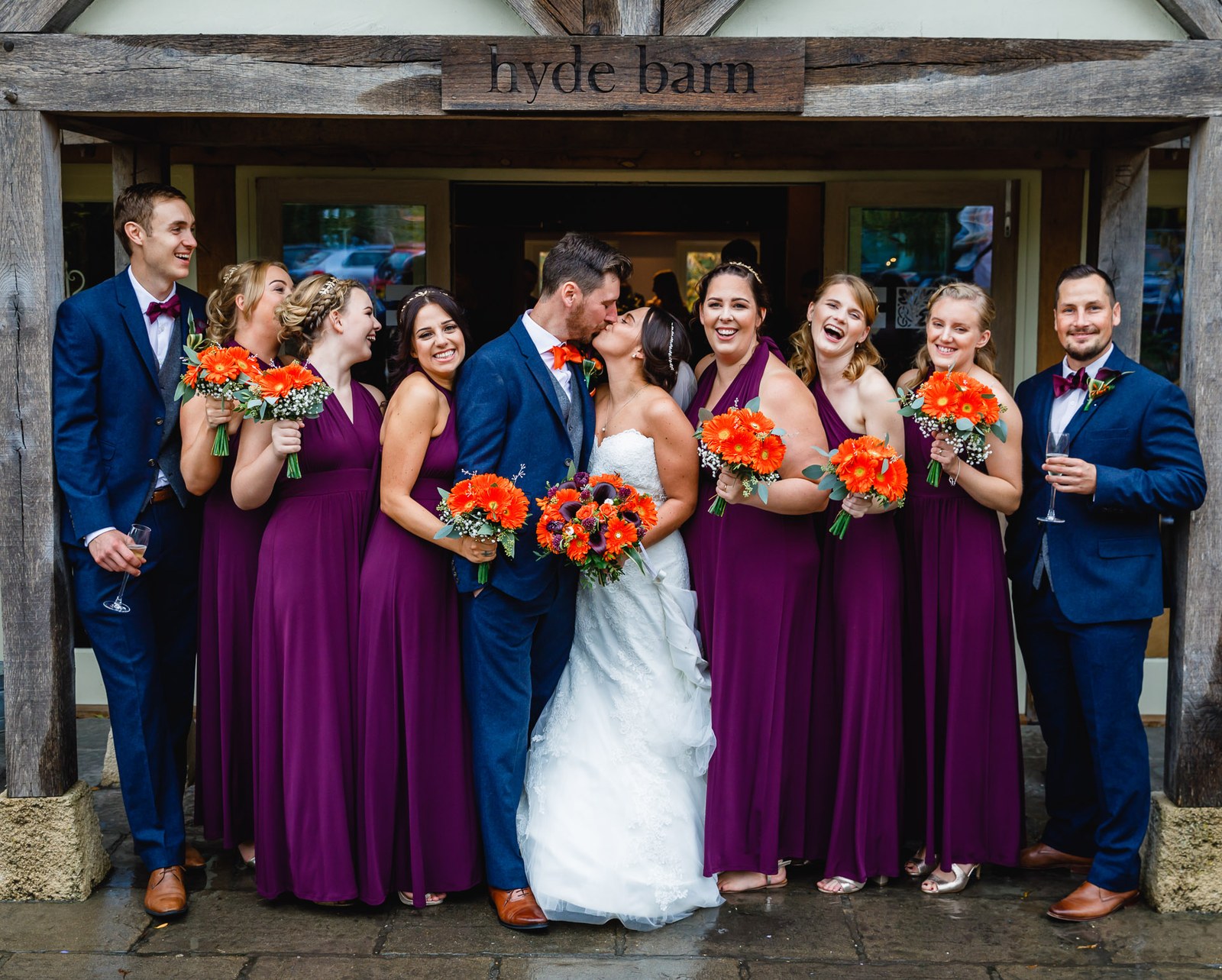 The full wedding party gathered beneath the timbered entrance of Hyde House