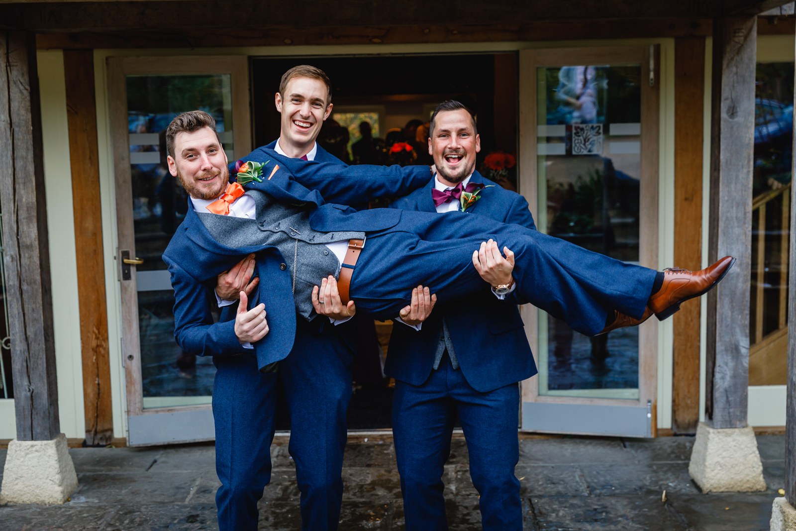 The groom and a groomsman carrying a third man aloft in high spirits