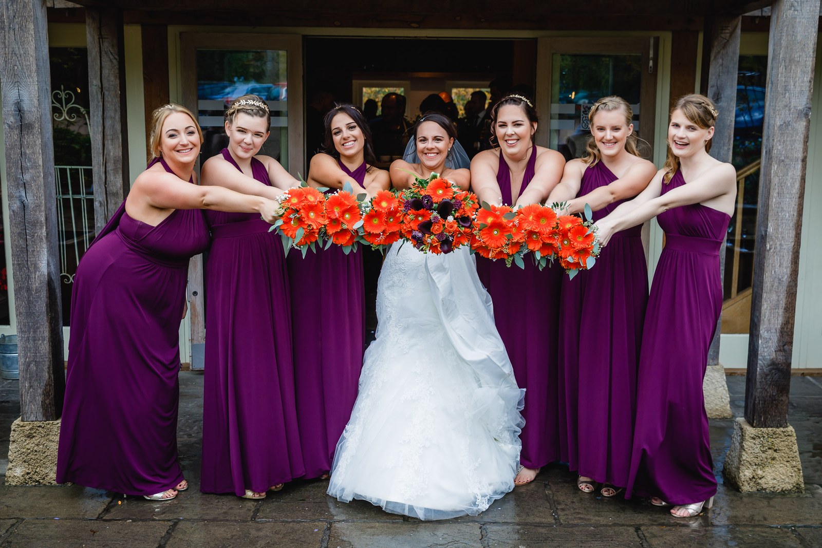 The bride and bridesmaids holding out their orange bouquets under the barn entrance