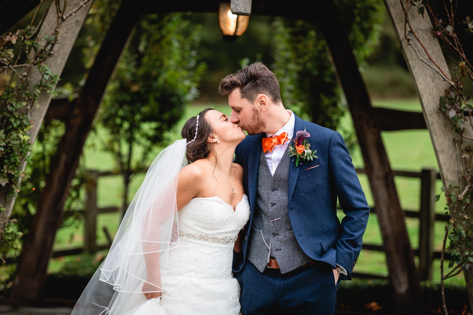The couple kissing beneath the oak-framed garden arbour at Hyde House