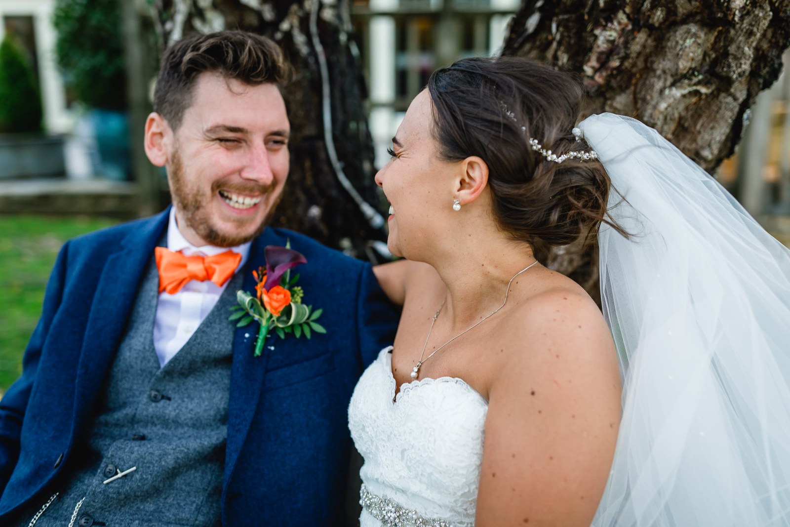 The couple laughing together beneath a tree in the grounds