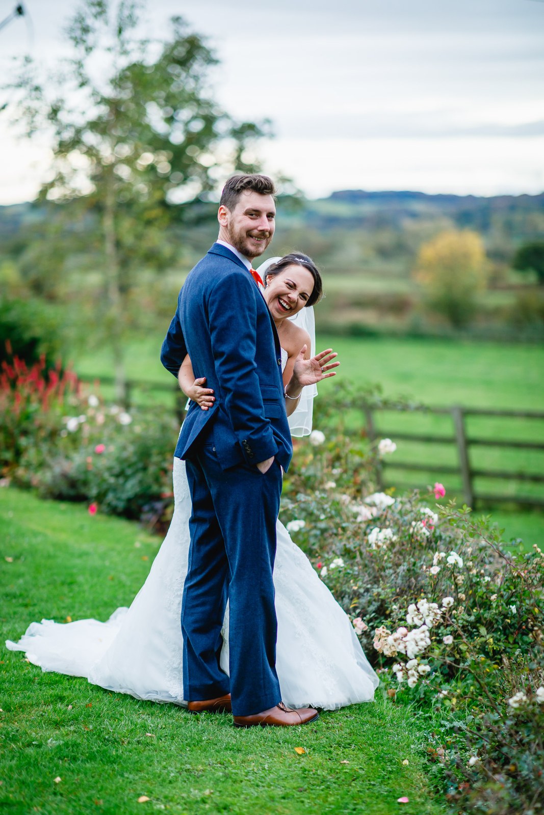 Bride and groom embracing among the rose beds with countryside beyond