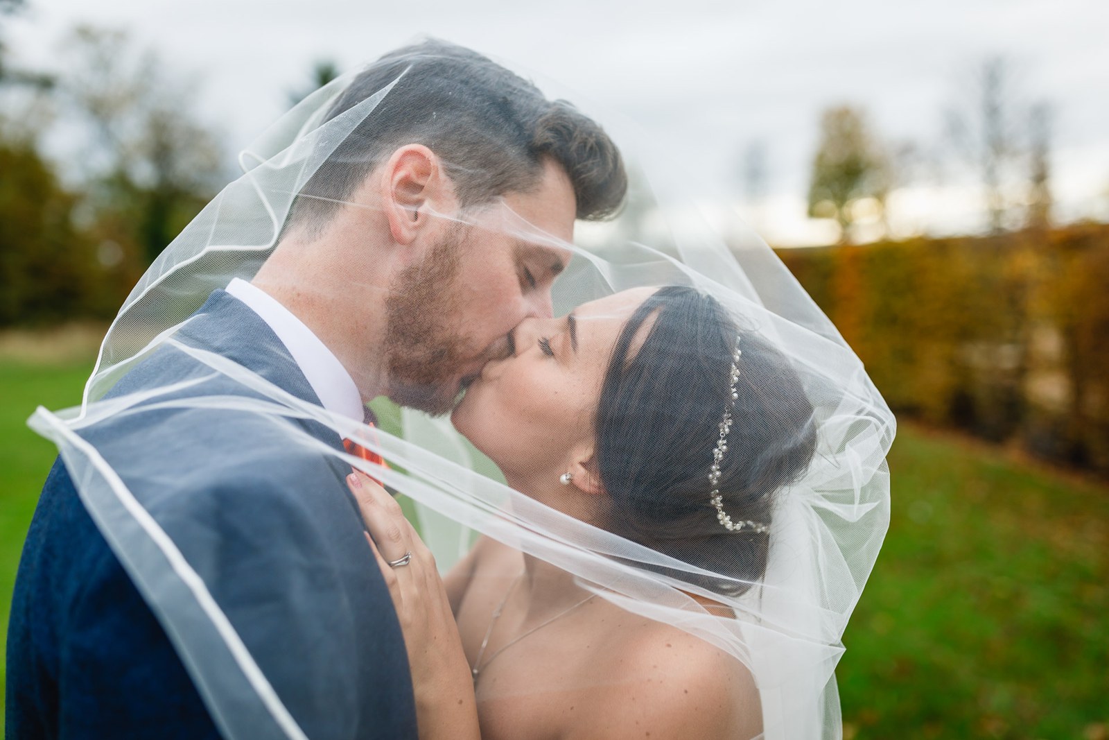 The couple kissing beneath the bride's veil among the autumn trees