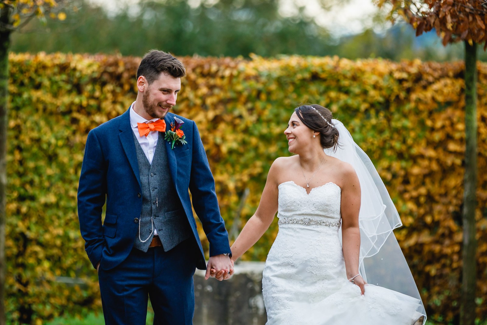 Bride and groom holding hands beside the golden autumn beech hedge