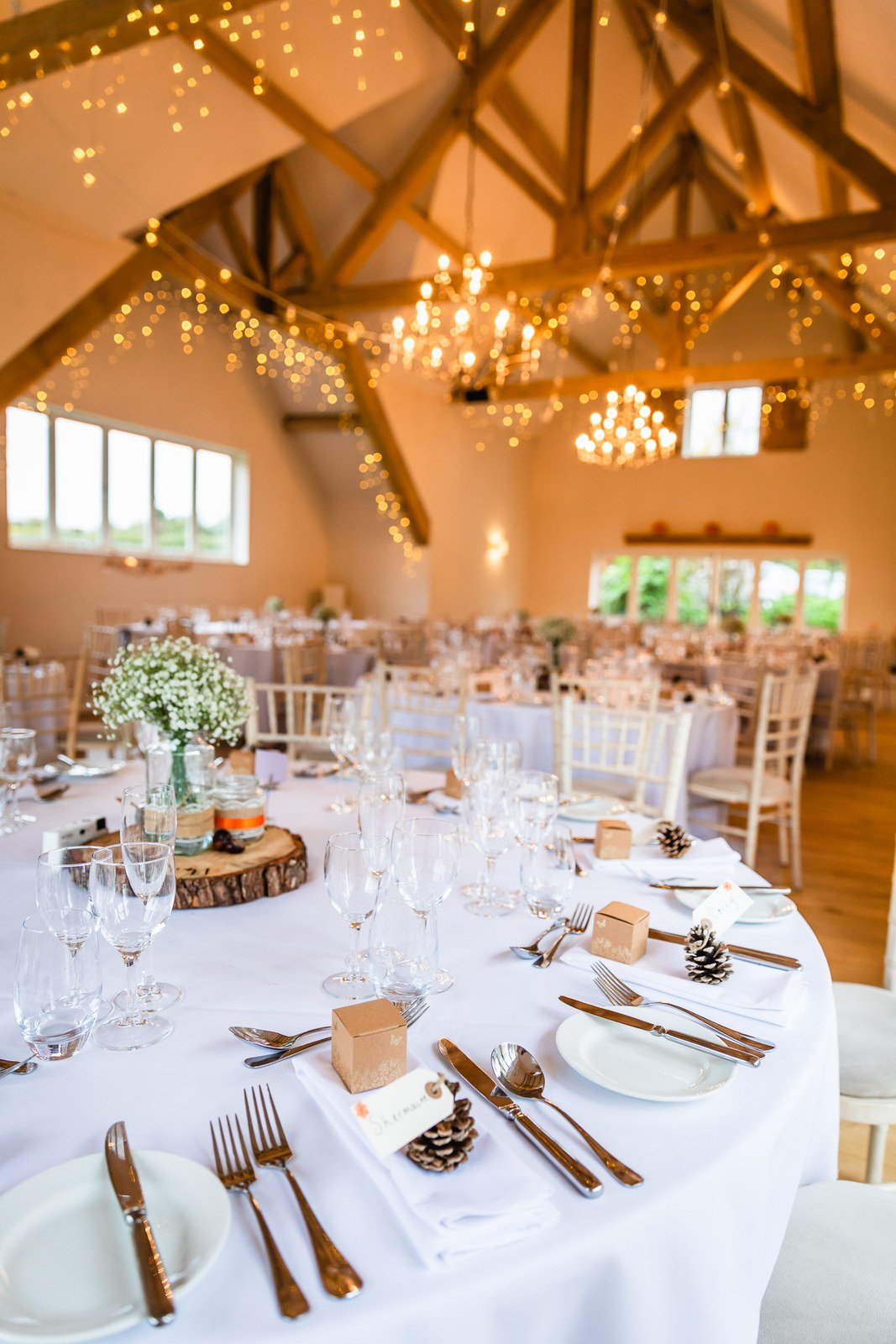 The reception barn at Hyde House laid with round tables beneath fairy-lit oak trusses