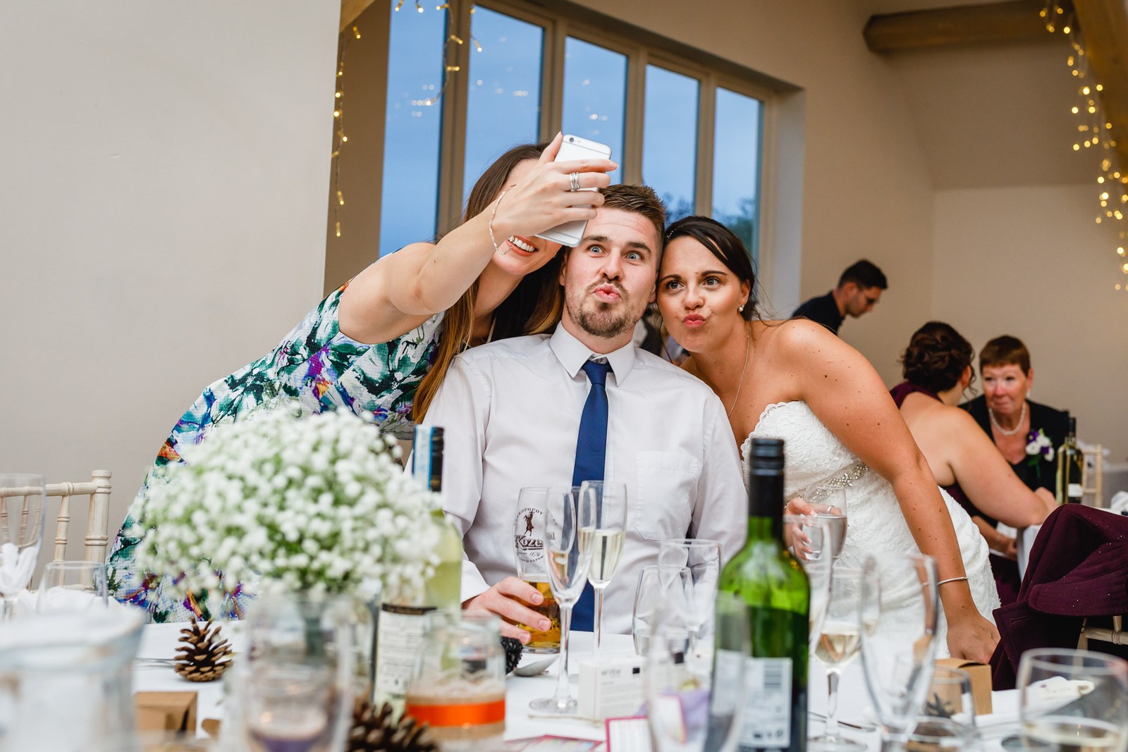 A guest leaning in to take a selfie with the bride at the table