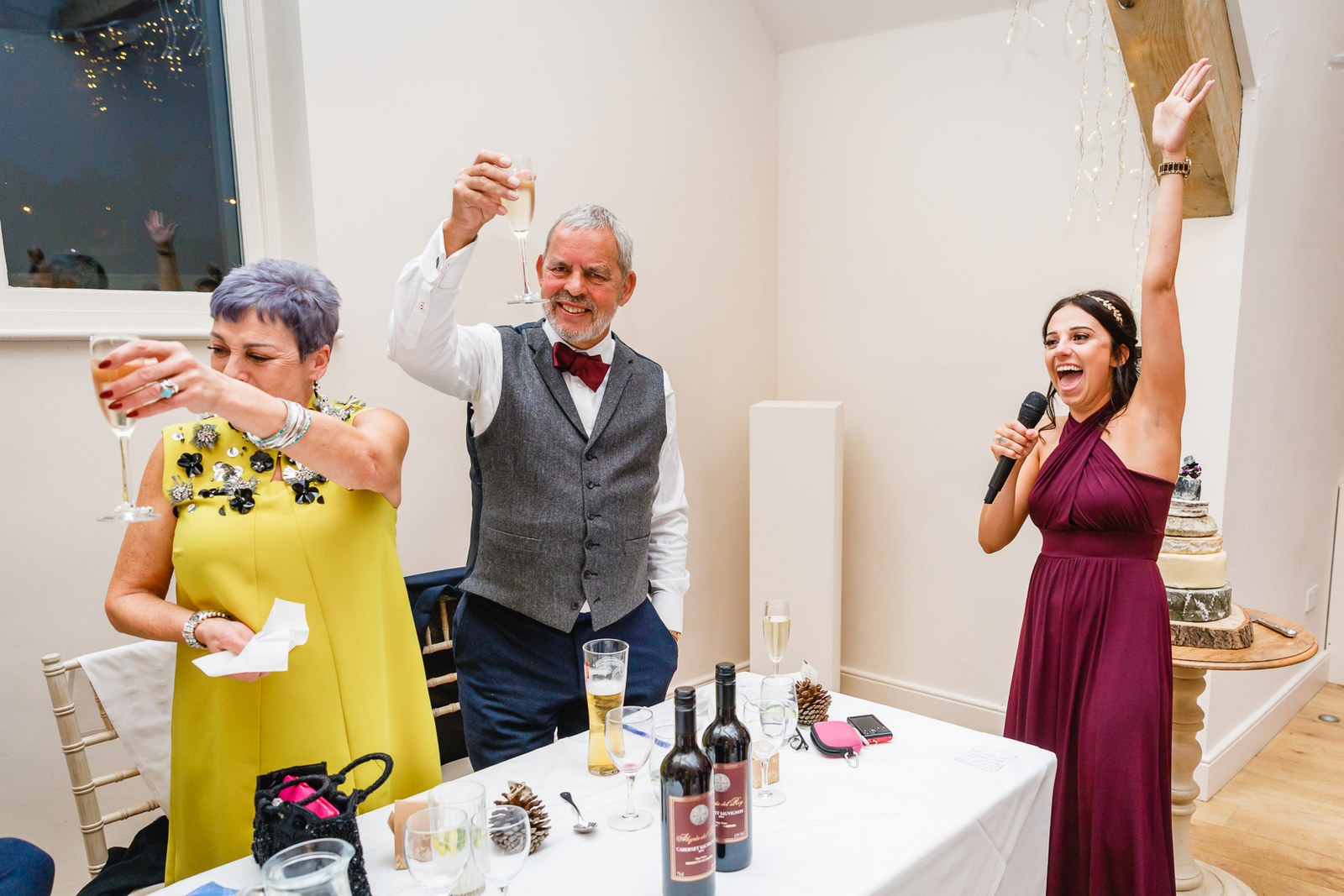 A guest raising a glass as a bridesmaid takes the microphone during the toasts