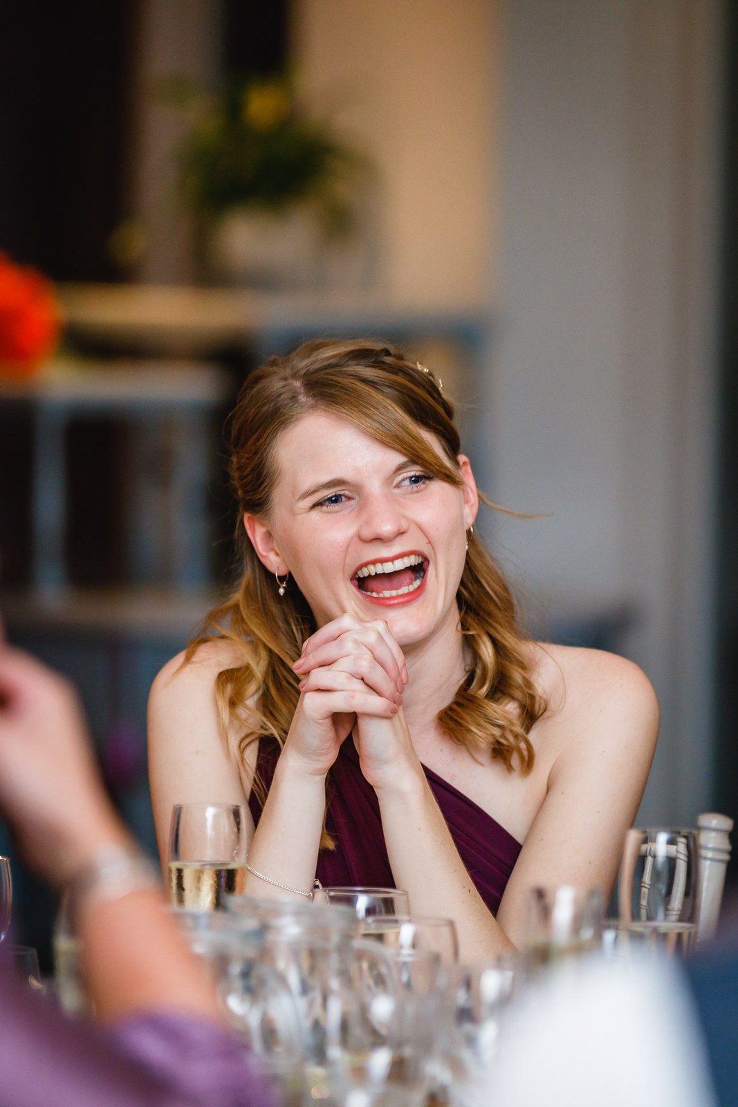 A bridesmaid laughing with hands clasped during the speeches