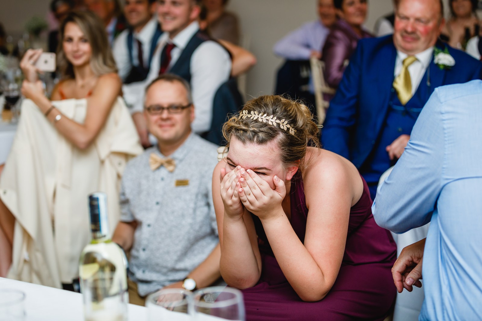 A bridesmaid hiding her face laughing as guests watch the speeches