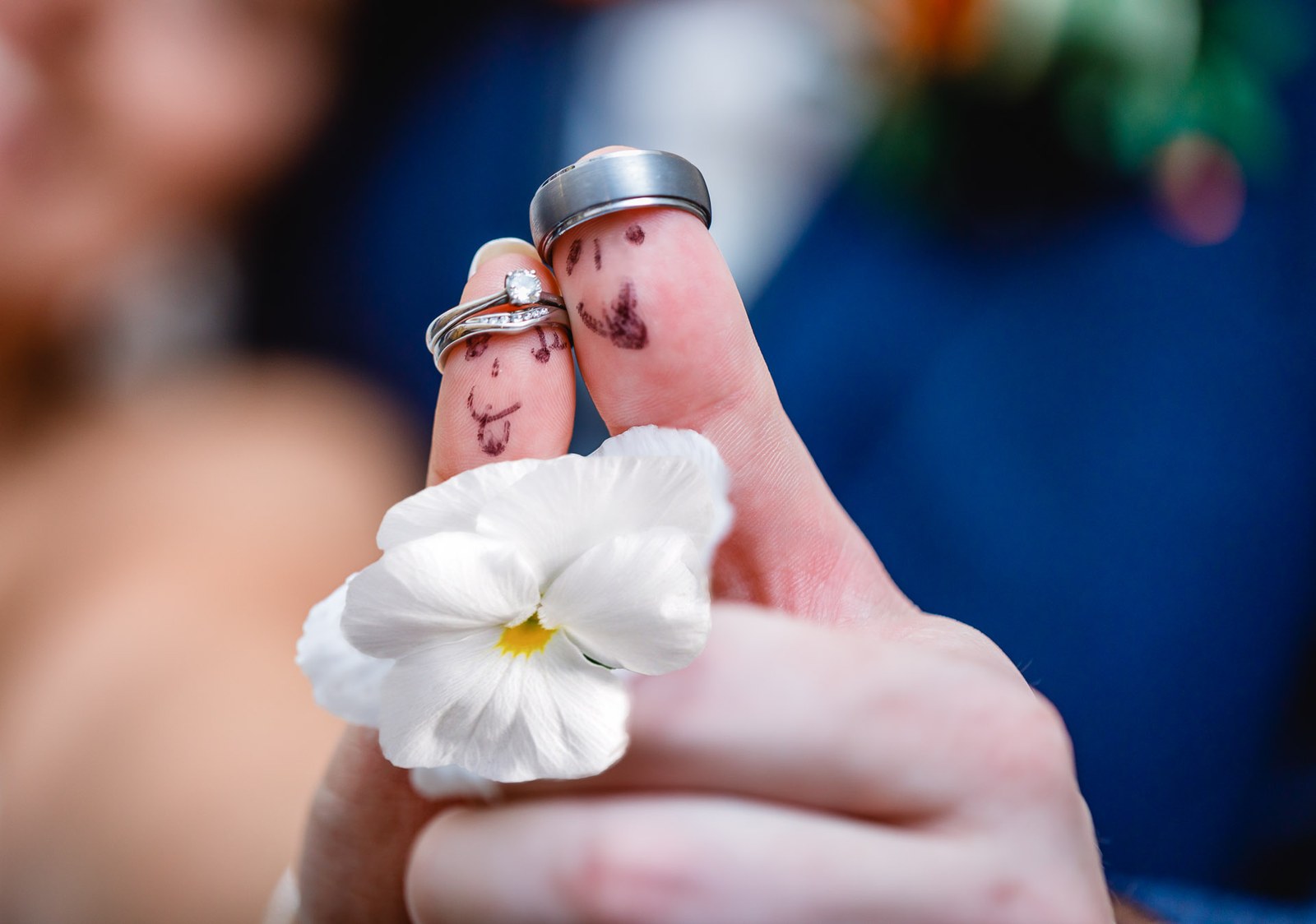 Close-up of the couple's ringed hands, fingers inked in fun, holding a single pansy