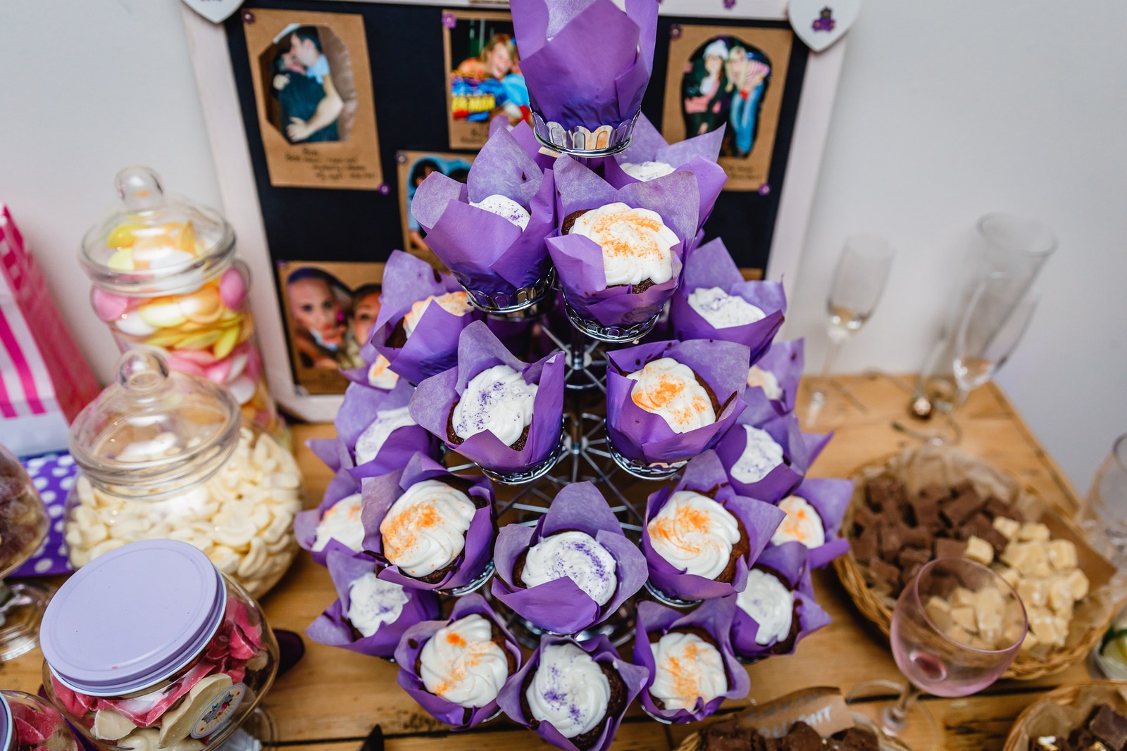 A tower of purple-wrapped cupcakes on the sweet table beside framed photos