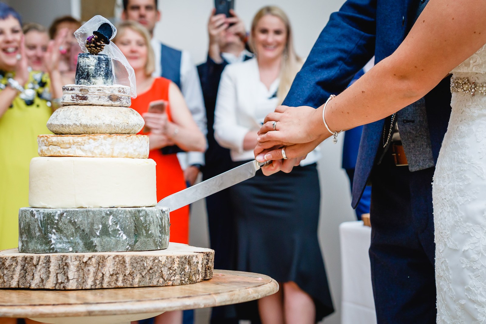 The couple cutting into their tiered cheese-wheel cake as guests watch