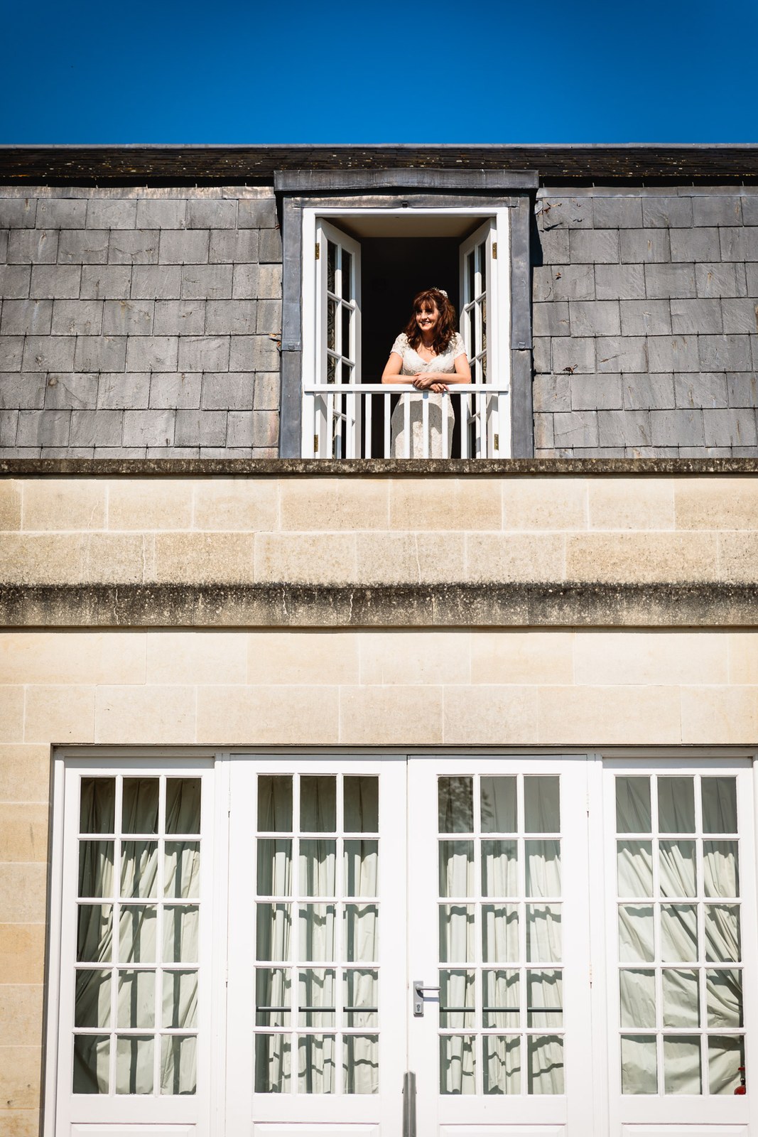 Bride leaning from an upper window of the honey-stone frontage of Leigh Park Country House Hotel