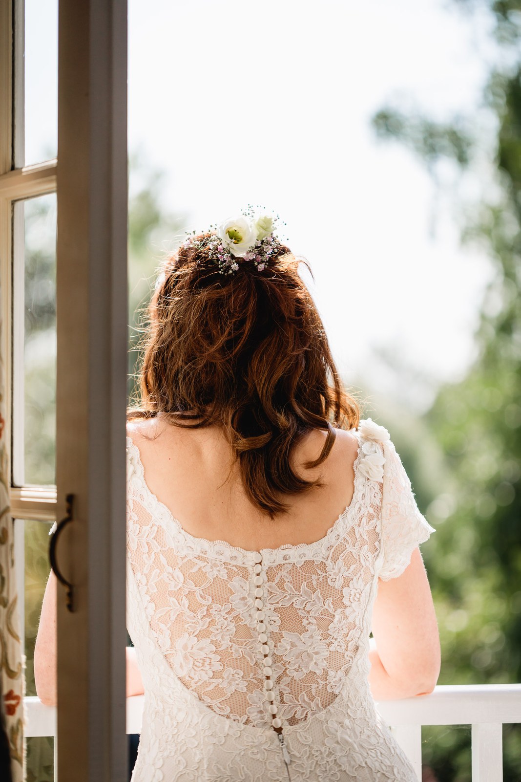 Bride from behind showing the lace button back of her gown by a bright window