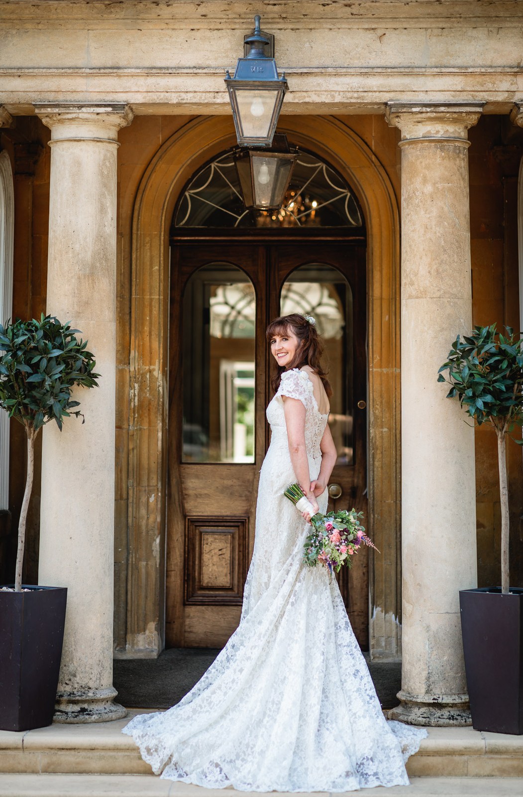 Bride by the columned entrance of the hotel, a lantern glowing above the door