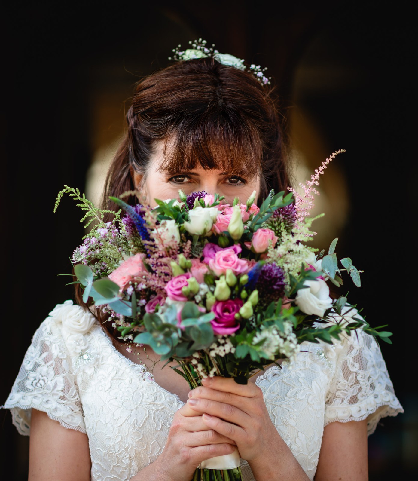 Bride holding her colourful bouquet of roses and lisianthus up to her face