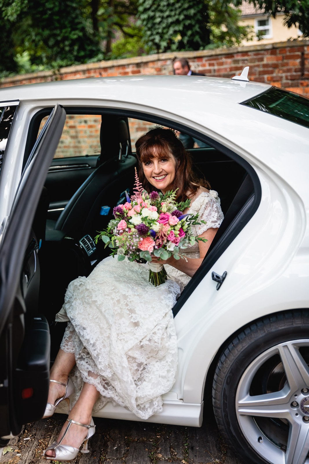 Bride stepping from the white wedding car holding her bouquet