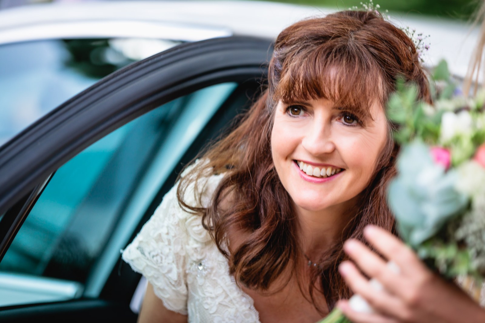 Bride emerging from the wedding car with a broad smile