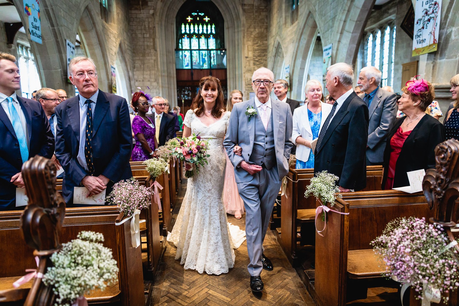 Bride walking down the aisle on her father's arm as guests stand, gypsophila on the pews