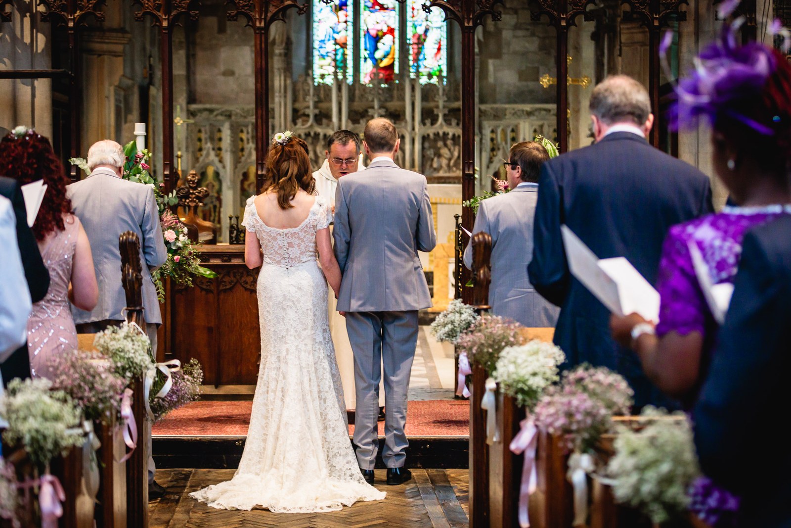 Bride from behind beside the groom at the altar, gypsophila decorating the pew ends