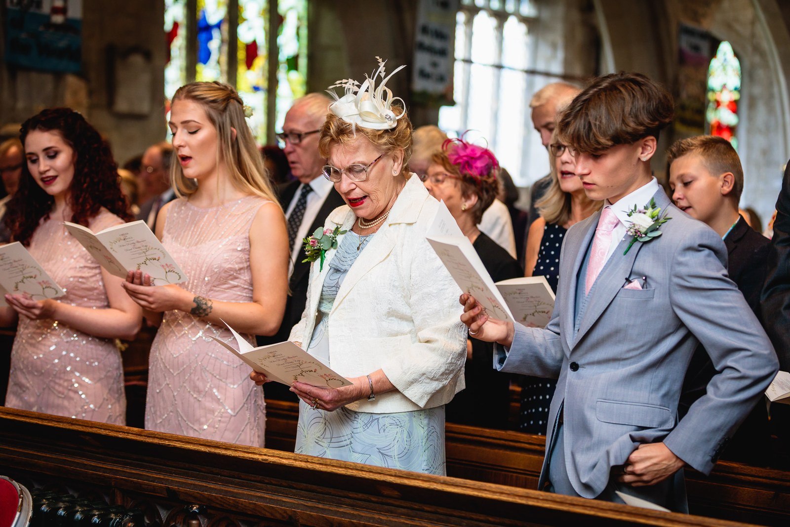 Bridesmaids and guests singing from order-of-service sheets during the ceremony