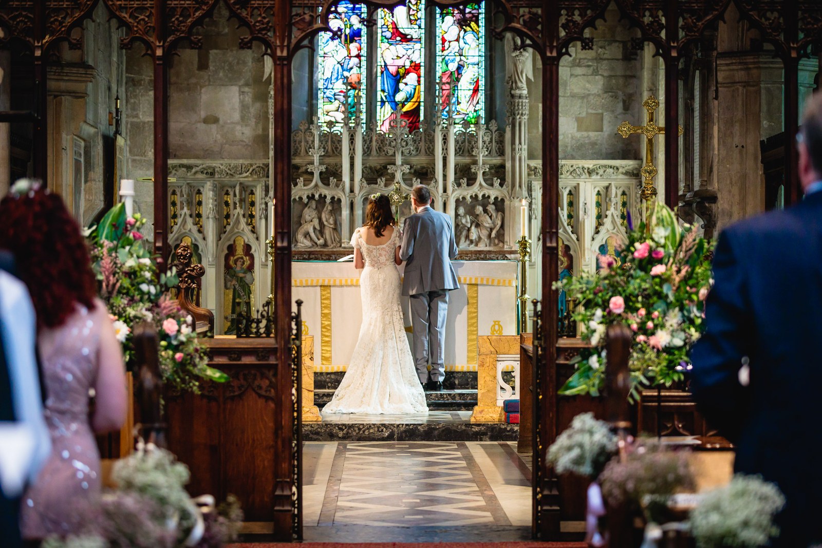 Bride and groom from behind at the altar below an ornate carved screen and stained glass