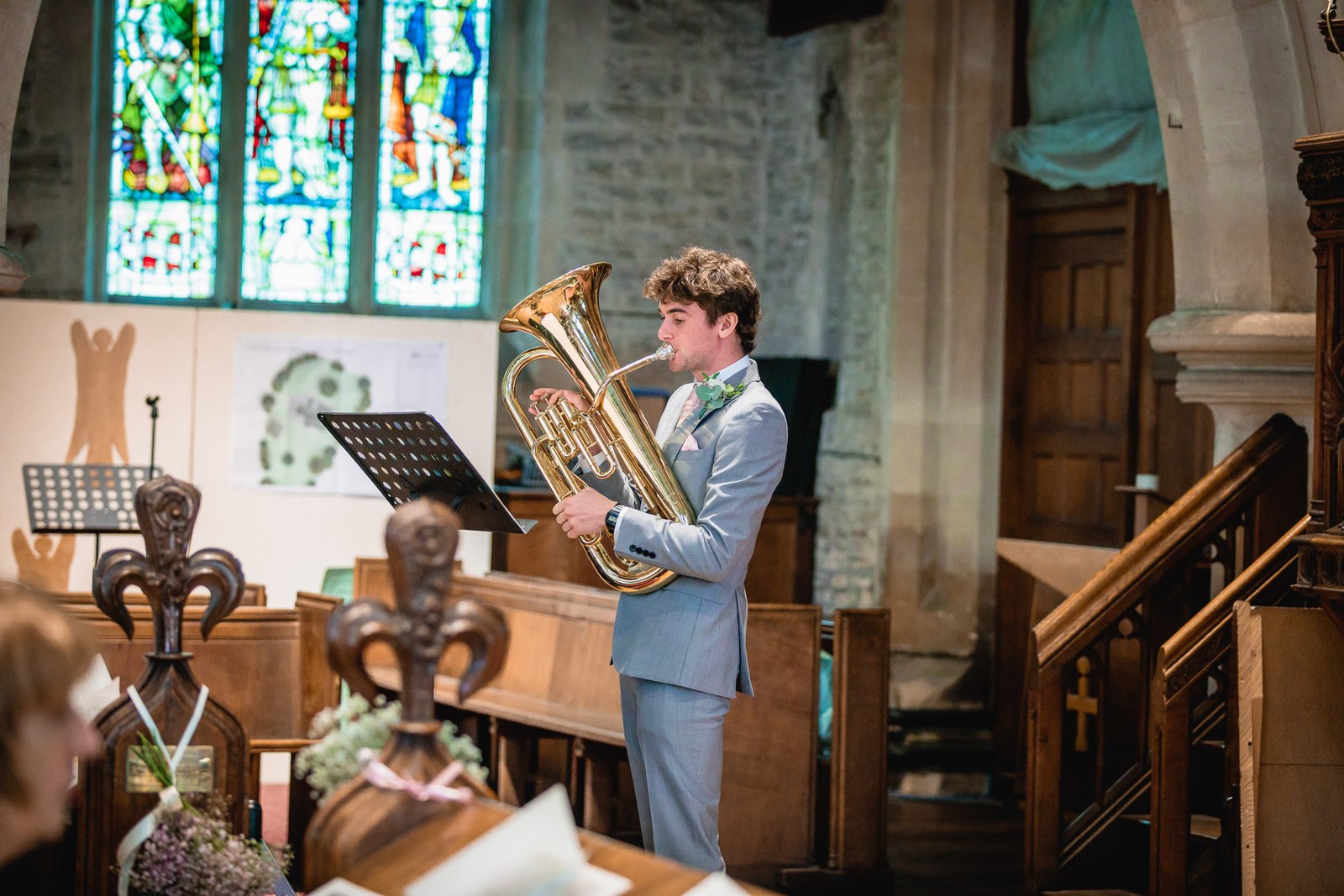 A guest in a grey suit playing a euphonium during the church ceremony