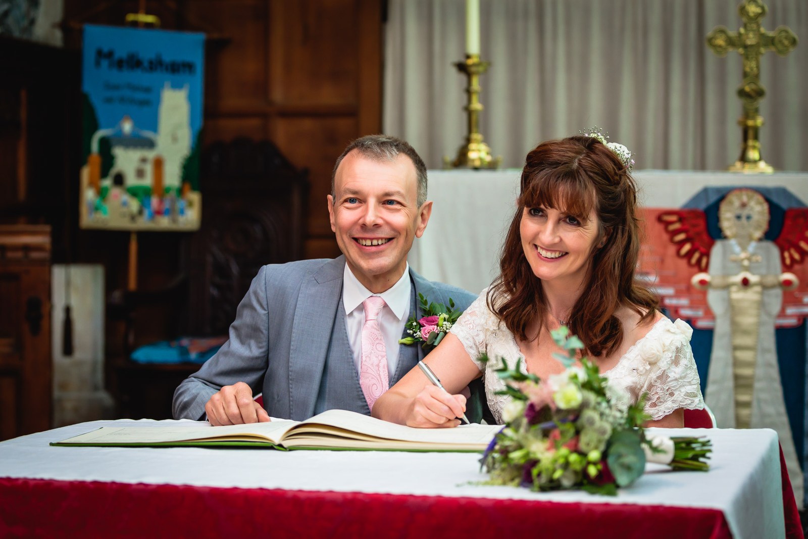 Bride and groom signing the register at a flower-topped table