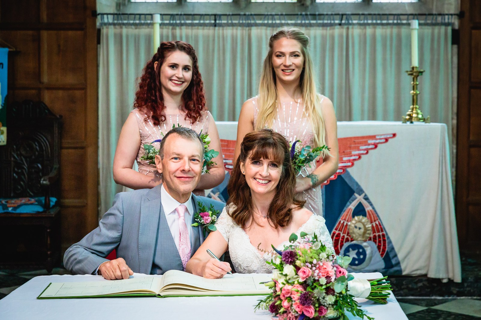The couple signing the register with two smiling bridesmaids standing behind