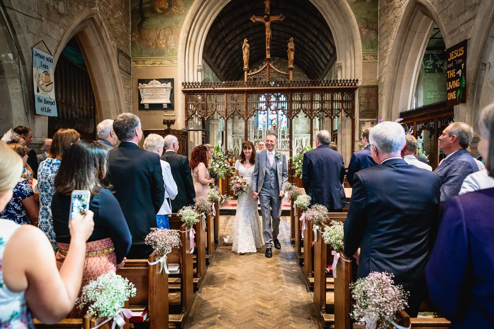The newlyweds walking back down the aisle as a guest films on a phone
